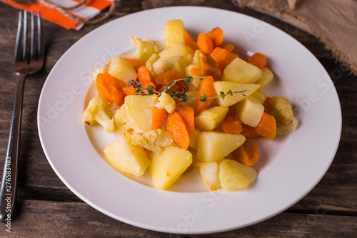 Boiled potatoes with vegetables and carrots on white plate on rustic wood table