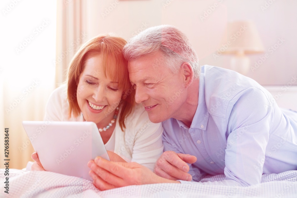 Smiling mature couple sharing digital tablet while lying on bed at home