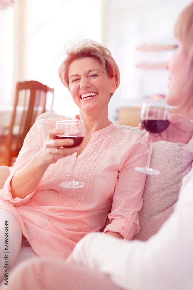 Cheerful mature friends with drinks sitting on sofa at home Cheerful mature friends with drinks sitting on sofa at home