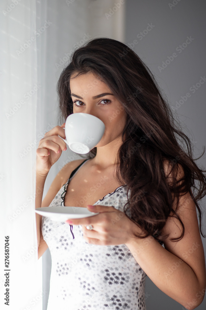 Sexy woman with cup in hand standing in room in front wall and beside window Sexy woman with cup in hand standing in room in front wall and beside window