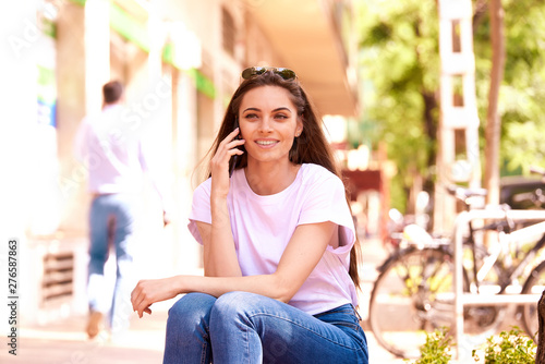 Portrait shot of attractive young woman sitting on the bench and talking with somebody on her mobile phone