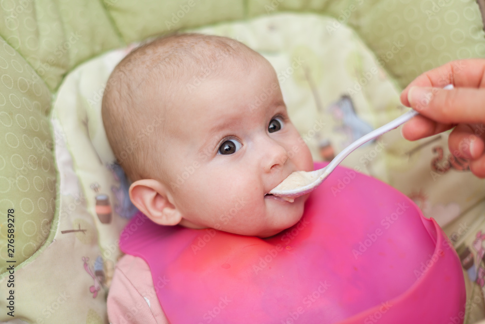 mother gives baby food from a baby spoon. baby eating food first time. weaning baby mother gives baby food from a baby spoon. baby eating food first time. weaning baby