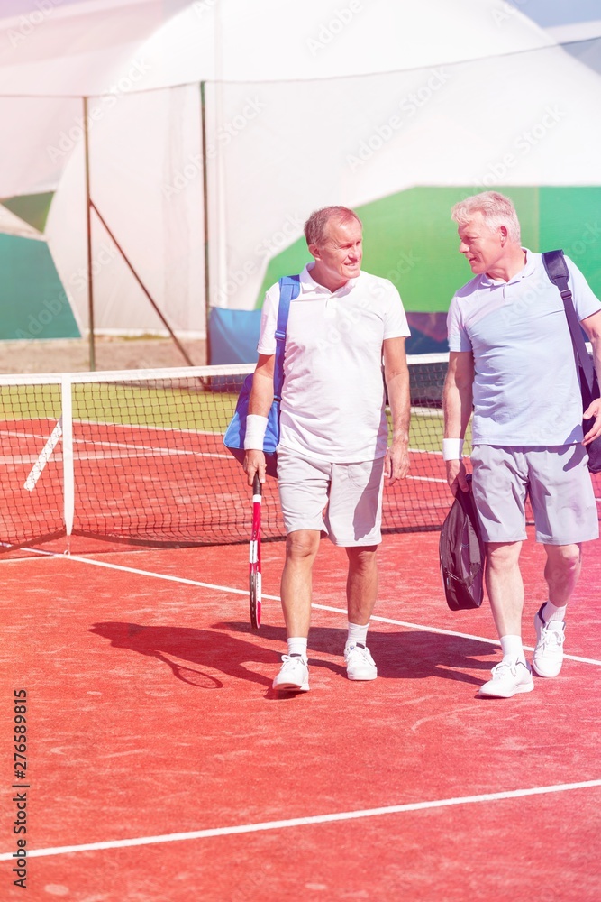 Full length of men in sports clothing talking while walking on tennis court during summer weekend