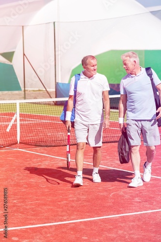 Full length of men in sports clothing talking while walking on tennis court during summer weekend