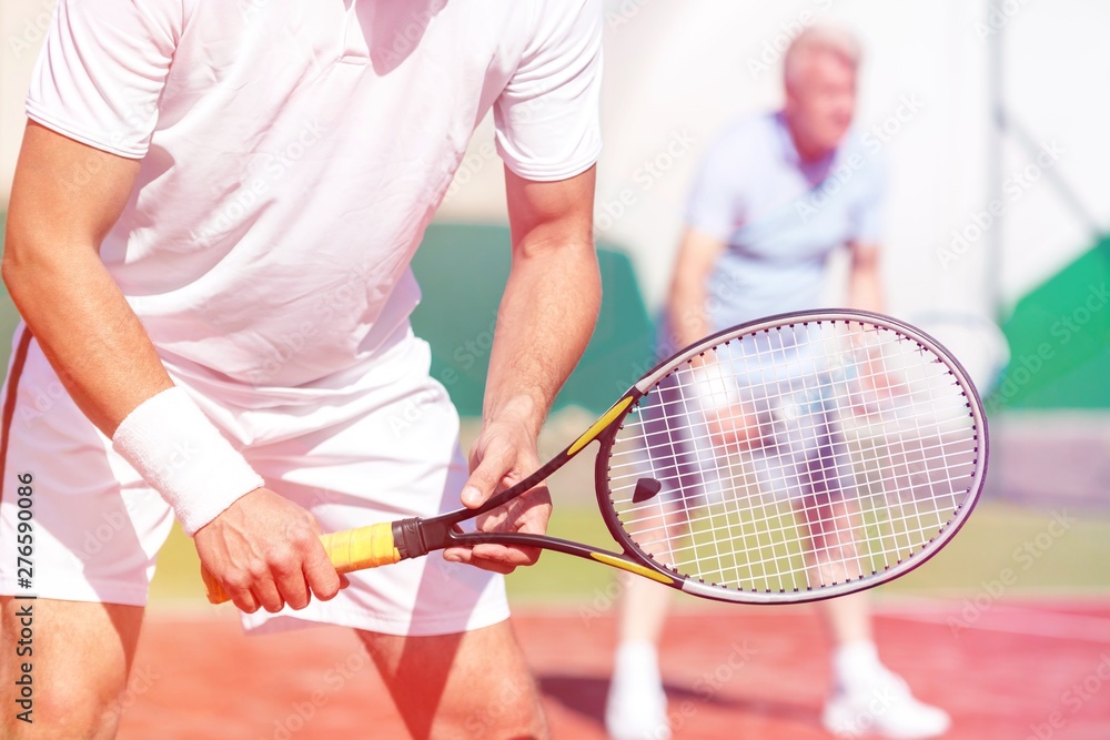 Midsection of man standing with tennis racket against friend playing doubles match on court