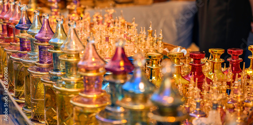 Close together standing richly decorated and colored perfume flacons made of glass in the light of the setting sun.