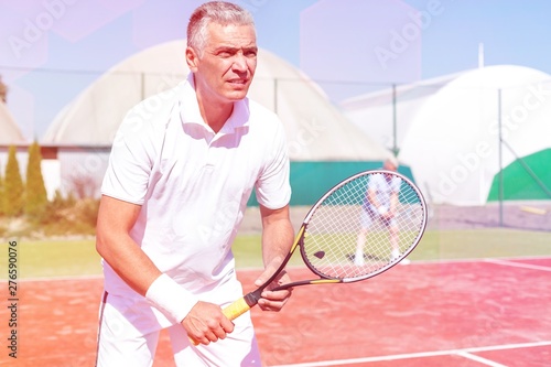 Confident mature man standing with tennis racket against friend playing doubles match on court