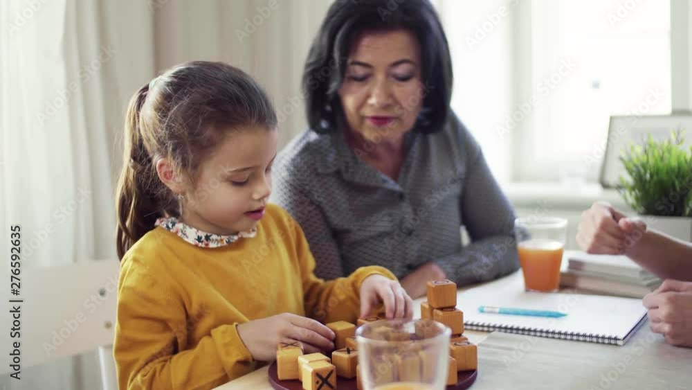 A small girl with mother and grandmother sitting at table at home, playing games. A small girl with mother and grandmother sitting at table at home, playing games.