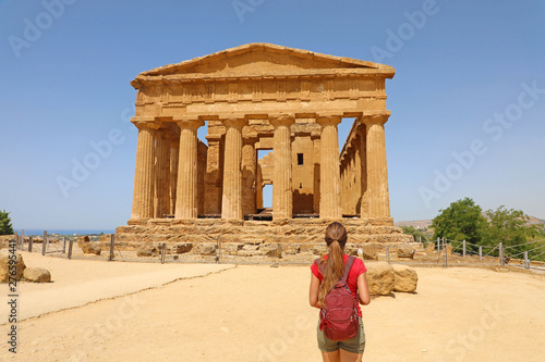 Young woman looks at Concordia Temple in the Valley of the Temples Agrigento, Sicily. Traveler girl visits Greek Temples in Southern Italy.