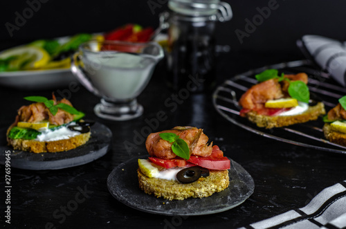 small canape with pink salmon fish, cucumber, tomato, olive and lemon on a black background. dark food photo