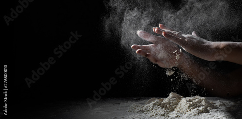 woman chef hand clap with splash of white flour and black background with copy space. © pavel siamionov