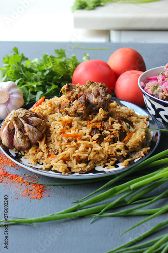 Pilaf on a platter of meat and spices.pilaf in a plate on a wooden background, top view.  The concept of Oriental cuisine. Homemade Uzbek pilaf of lamb is served in cast iron cookware. Copy space.