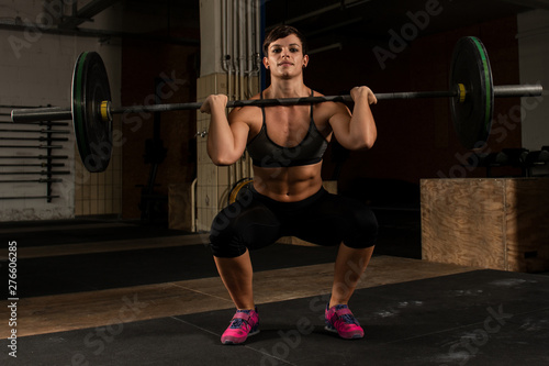 Junge muskulöse Frau mit kurzen Haaren beim Workout mit der Langhantel. Die hübsche athletische Sportlerin macht Kniebeugen mit der Langhantel. Krafttraining mit Gewichten. Schwarz und weiß.