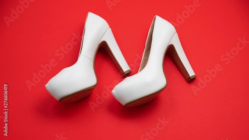 Pair of white high heeled shoes moving backwards, isolated on red studio background. Moseying back - uncomfortable fashion - dancing and backtracking stop motion concept photo