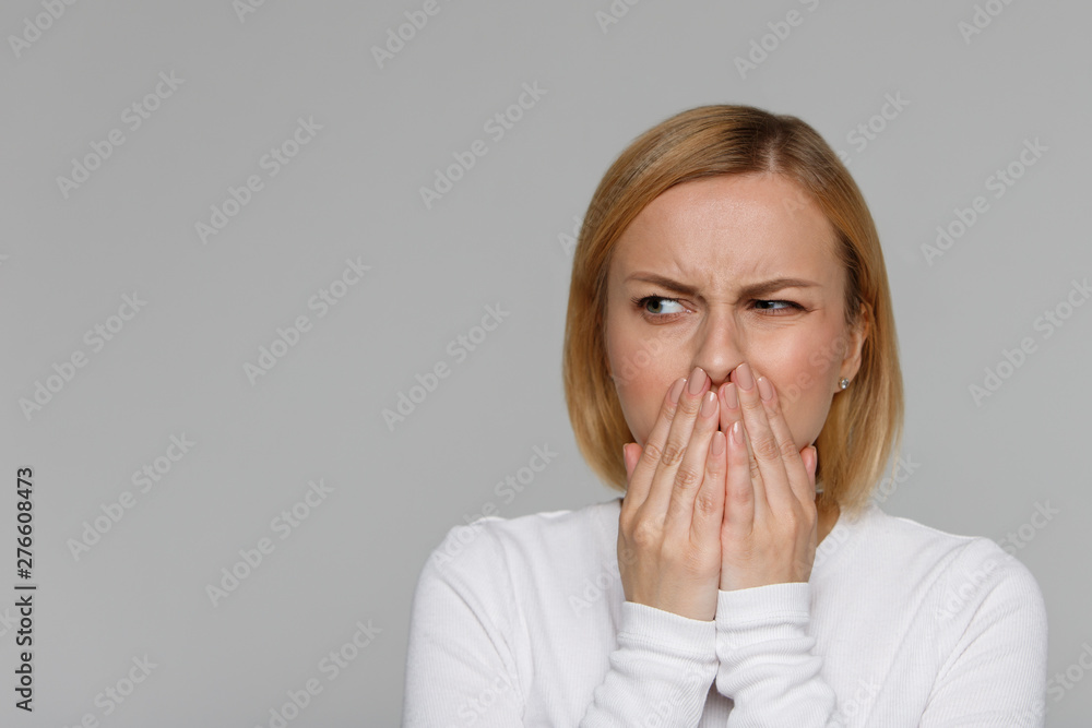 Studio portrait of unhealthy cute blonde female covers nose with hands, looks to the source of the allergy or unpleasant smell, contaminated air, dust. I do not like Studio portrait of unhealthy cute blonde female covers nose with hands, looks to the source of the allergy or unpleasant smell, contaminated air, dust. I do not like
