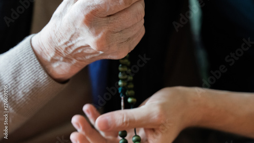 young man hand holding elderly woman hand with rosary beads. family care, praying concept. risk group coronavirus or covid virus