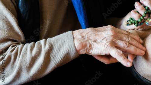 young man hand holding elderly woman hand with rosary beads. family care, praying concept. risk group coronavirus or covid virus