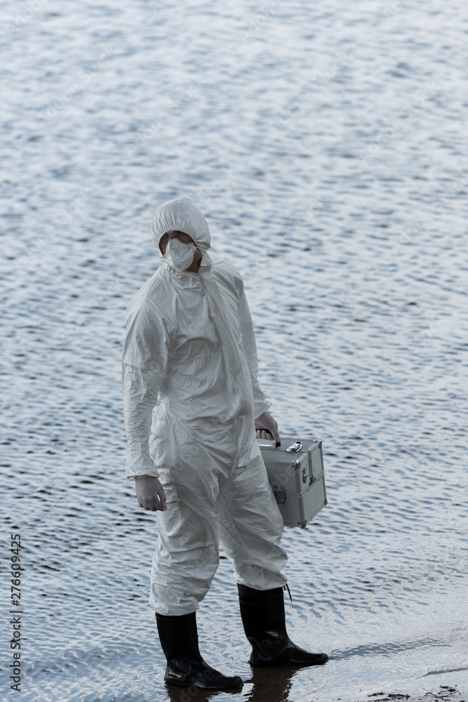 full length view of water inspector in protective costume holding inspection kit at river full length view of water inspector in protective costume holding inspection kit at river