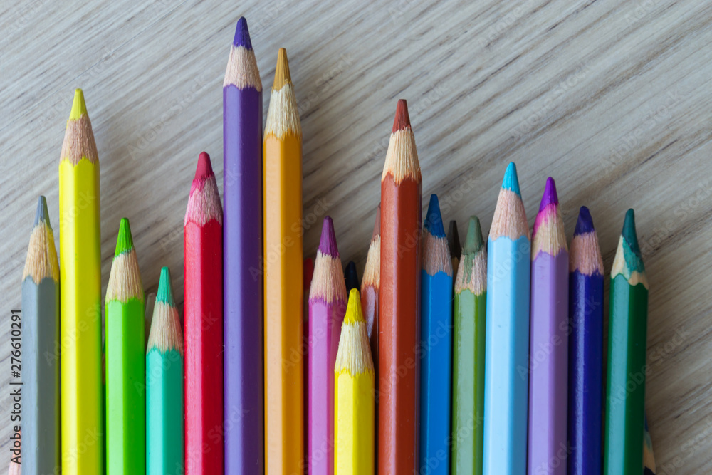 The group of a different length colored drawing pencils are laying on the wooden desk background and waiting for a painting lesson. The group of a different length colored drawing pencils are laying on the wooden desk background and waiting for a painting lesson.