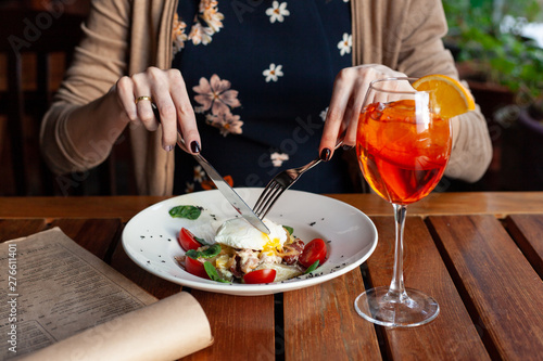 Woman is eating gourmet salad with poached egg with fork and knife on a summer terrace