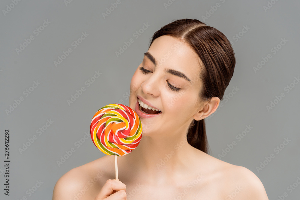 cheerful young woman looking at colorful lollipop isolated on grey