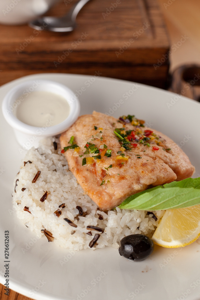 Steamed piece of salmon with boiled basmati rice in a white dish, served on a rustic wooden table