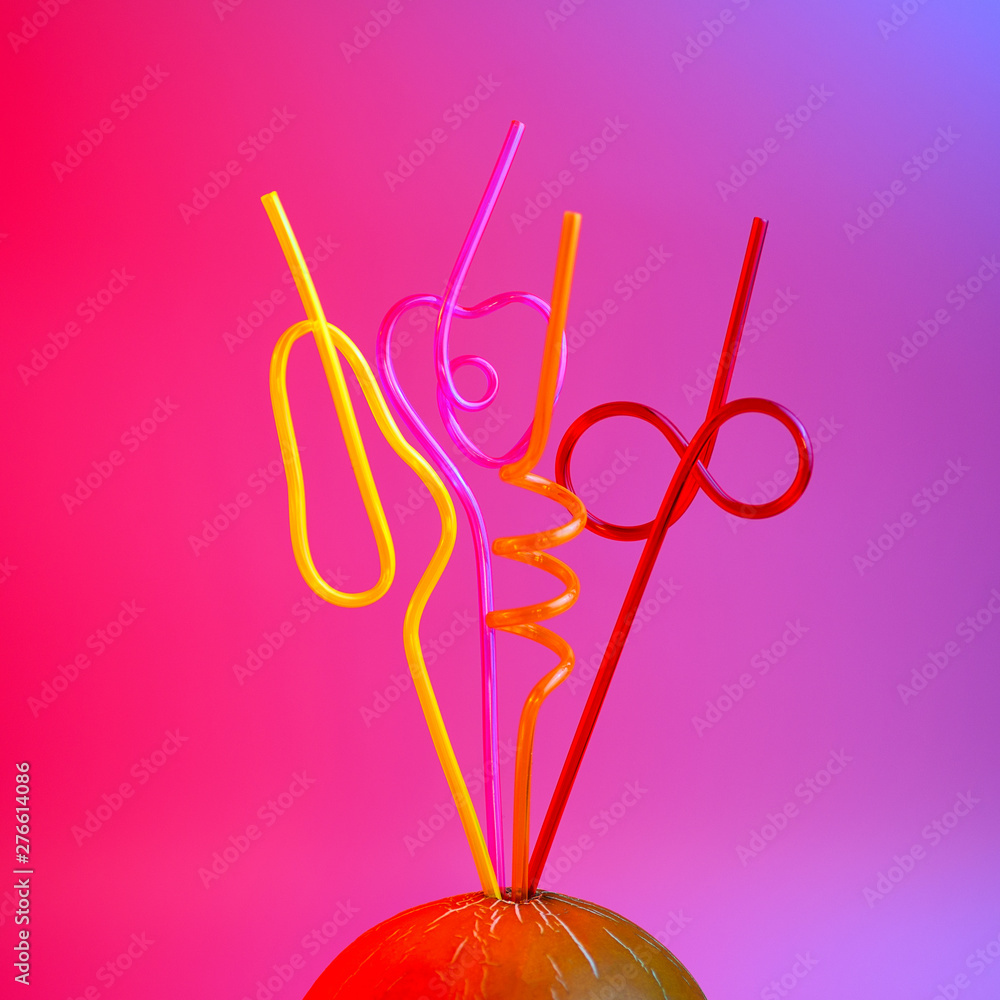 a bright colored cocktail tubes stuck in a melon on a pink background