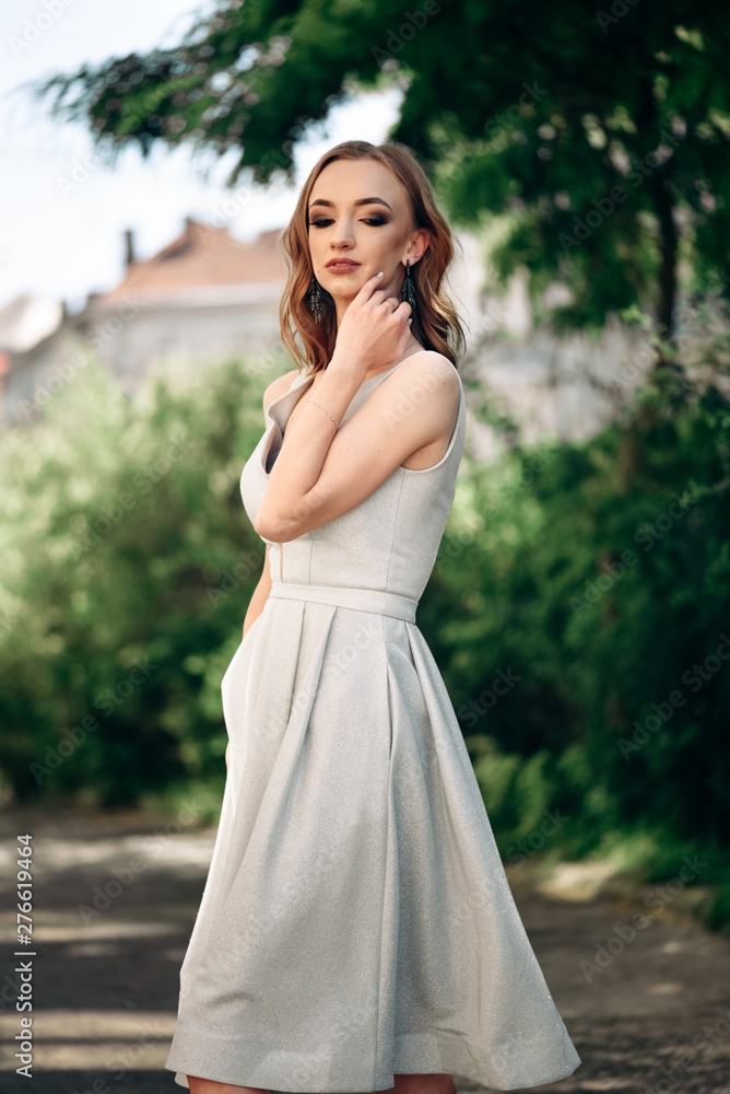 Gorgeous young model woman with perfect hair looking at camera posing in the city wearing evening dress. Gorgeous young model woman with perfect hair looking at camera posing in the city wearing evening dress.