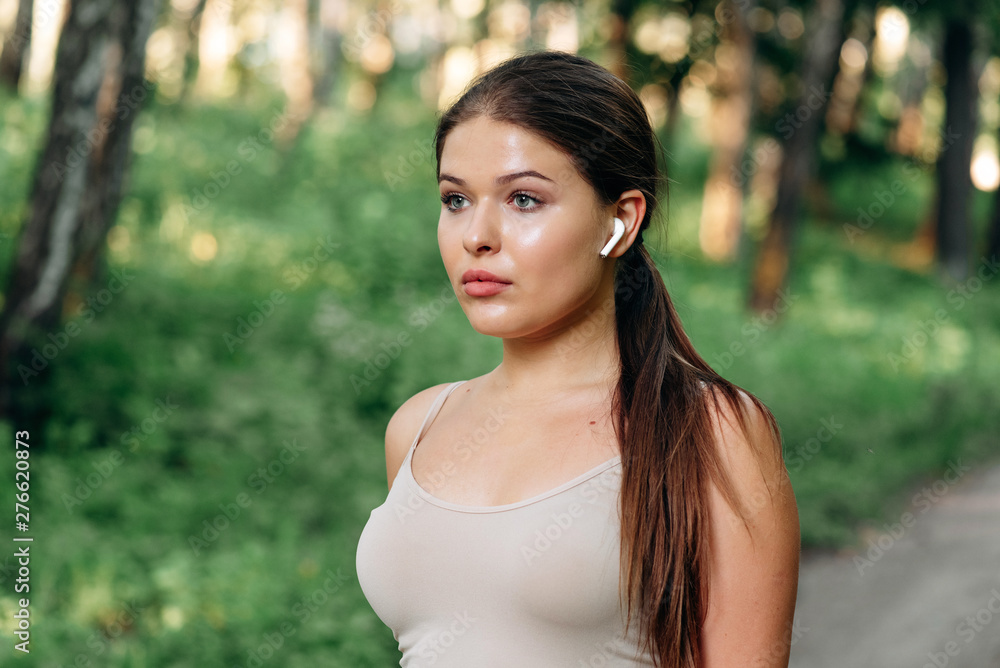 Close up portrait of a lovely young fitness girl listening to music through wireless earphones outdoors Close up portrait of a lovely young fitness girl listening to music through wireless earphones outdoors