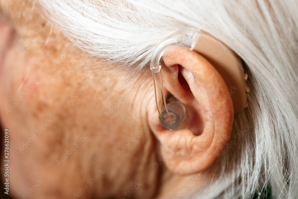 Closeup of a senior woman inserting a hearing aid in her hear. Focus on the hearing aid. Closeup of a senior woman inserting a hearing aid in her hear. Focus on the hearing aid.