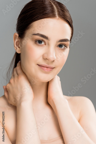 young naked woman touching neck and smiling isolated on grey