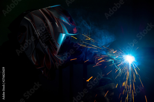 male welder in a mask performing metal welding. photo in dark colors. sparks flying.