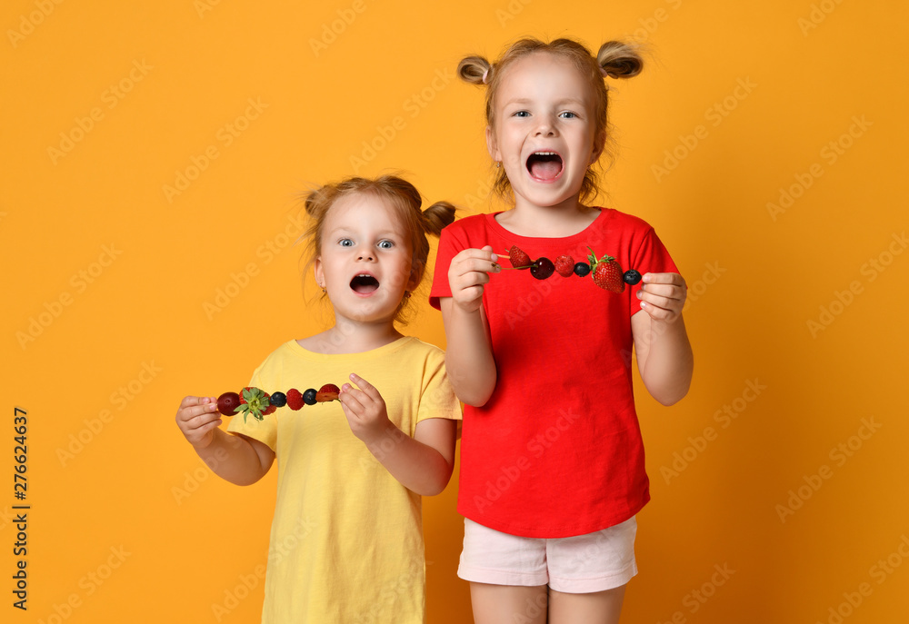 Two kids sisters happy smiling screaming in red tshirt hold fruit