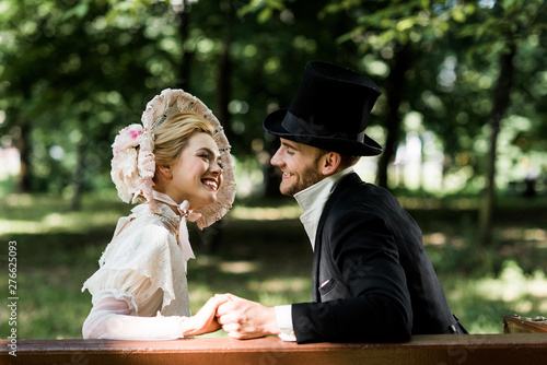 handsome aristocratic man holding hands with cheerful victorian woman in hat photo