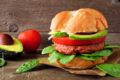 Plant based meatless burger with avocado, tomato and spinach against a rustic wood background