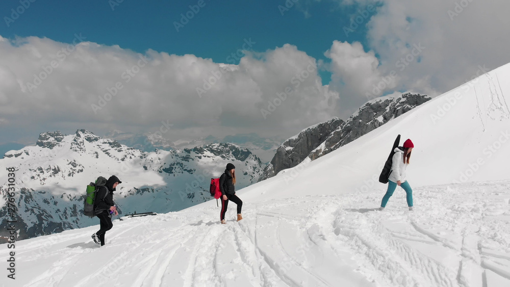 Three friends walking upwards on the snow in Dolomites with big backpacks