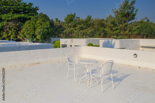 White metal table and chairs place on rooftop terrace surrounded with green trees at countryside.