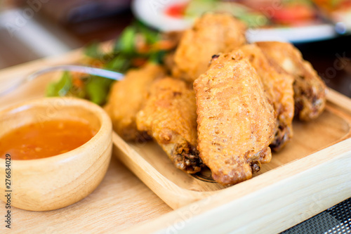 Fried crispy chicken pieces with sauce in wooden dish on table, Thailand.