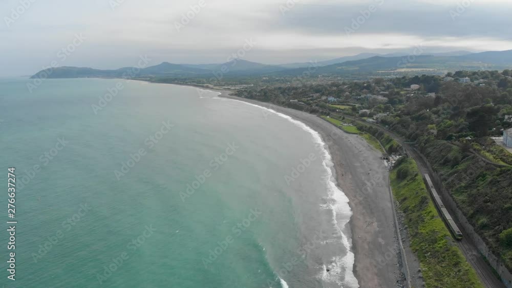 Panoramic ultrawide shot of train passing by the beautiful green sea on a bright sunny day with mountains in the background. Kiliney, Dublin, Ireland Panoramic ultrawide shot of train passing by the beautiful green sea on a bright sunny day with mountains in the background. Kiliney, Dublin, Ireland