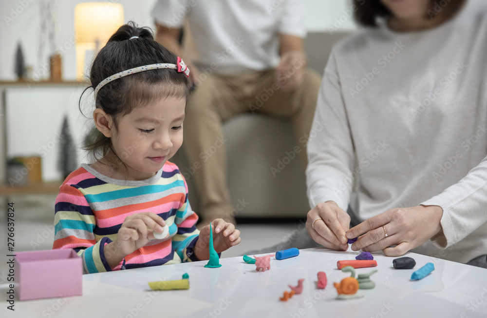 Mom with her daughter playing with a colorful toys modeling clay on the floor, at background daddy is sitting in a sofa in the living room, Happy asian family at home Mom with her daughter playing with a colorful toys modeling clay on the floor, at background daddy is sitting in a sofa in the living room, Happy asian family at home