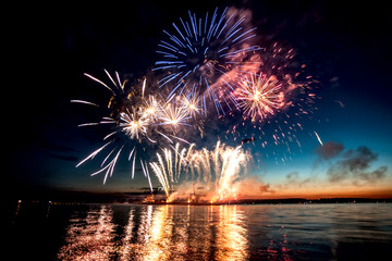 Holiday fireworks above water with reflection on the black sky background