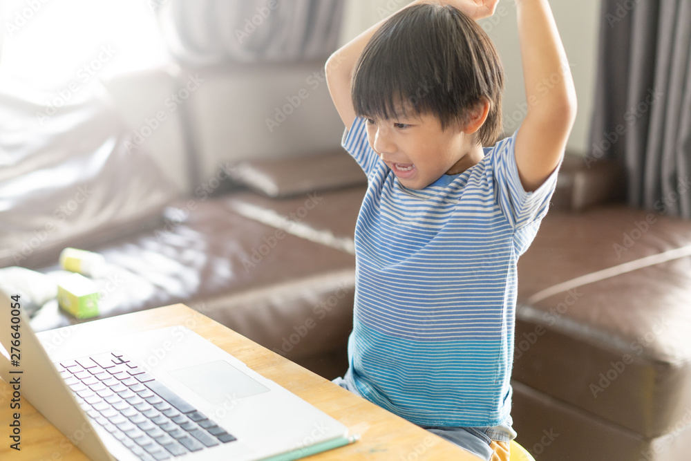 Happy asian boy in blue shirt using computer on wooden desk at home .Asian child smiling and happiness playing computer at room. Happy asian boy in blue shirt using computer on wooden desk at home .Asian child smiling and happiness playing computer at room.