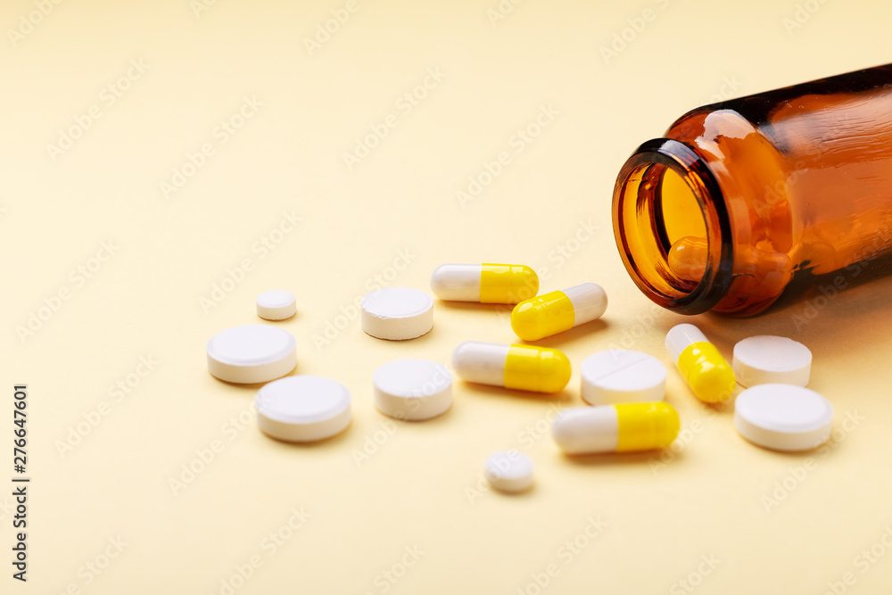 Multicolor tablets and pills capsules from glass bottle on yellow background Heap of assorted various medicine tablets and pills. Health care Close-up Copy space Multicolor tablets and pills capsules from glass bottle on yellow background Heap of assorted various medicine tablets and pills. Health care Close-up Copy space