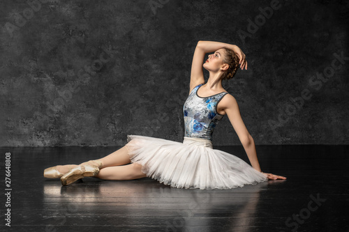 Ballerina. A young graceful ballerina dressed in professional attire, pointe shoes with ribbons and a white tutu, demonstrates dance skills while sitting on the studio floor. Beautiful classic ballet.