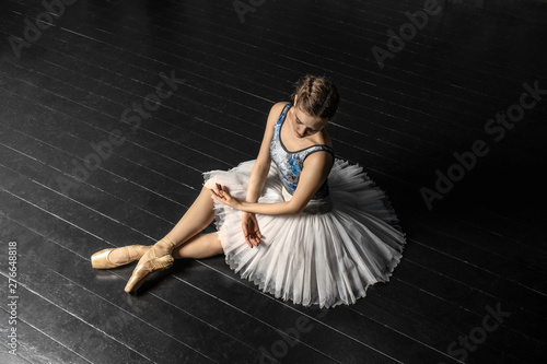 Ballerina. A young graceful ballerina dressed in professional attire, pointe shoes with ribbons and a white tutu, demonstrates dance skills while sitting on the studio floor. Beautiful classic ballet.