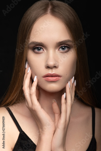 A beautiful young girl charmingly looks with blue eyes, lightly touches her hands to the face with a professional manicure. Advertising nail salon, Salon hairstyles & women barbershop and makeup.