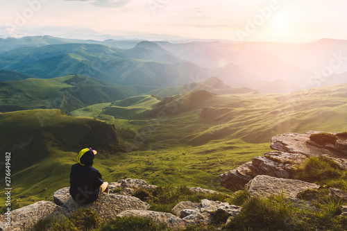 Canvas Print Travel man tourist sitting alone on the edge mountains over green valley adventu