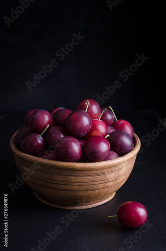 ripe plums in the bowl on black background