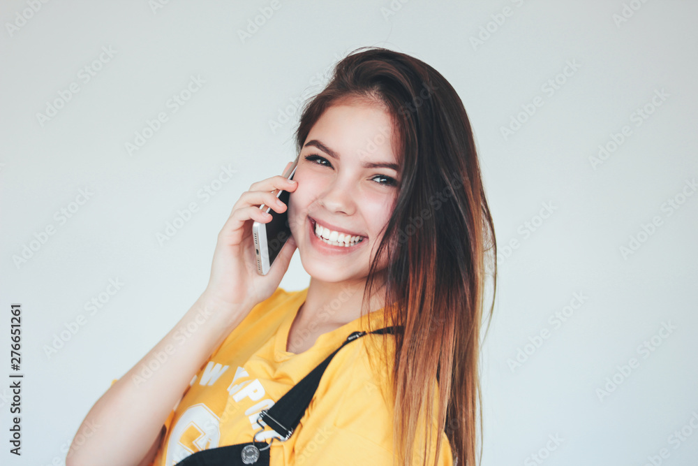 Portrait of happy carefree smiling teenager girl with dark long hair in yellow t-shirt using mobile isolated on grey background Portrait of happy carefree smiling teenager girl with dark long hair in yellow t-shirt using mobile isolated on grey background