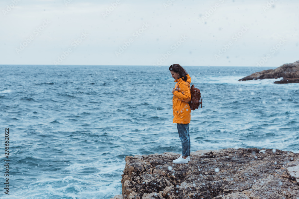 woman in yellow raincoat at the cliff enjoying sea view at stormy weather woman in yellow raincoat at the cliff enjoying sea view at stormy weather